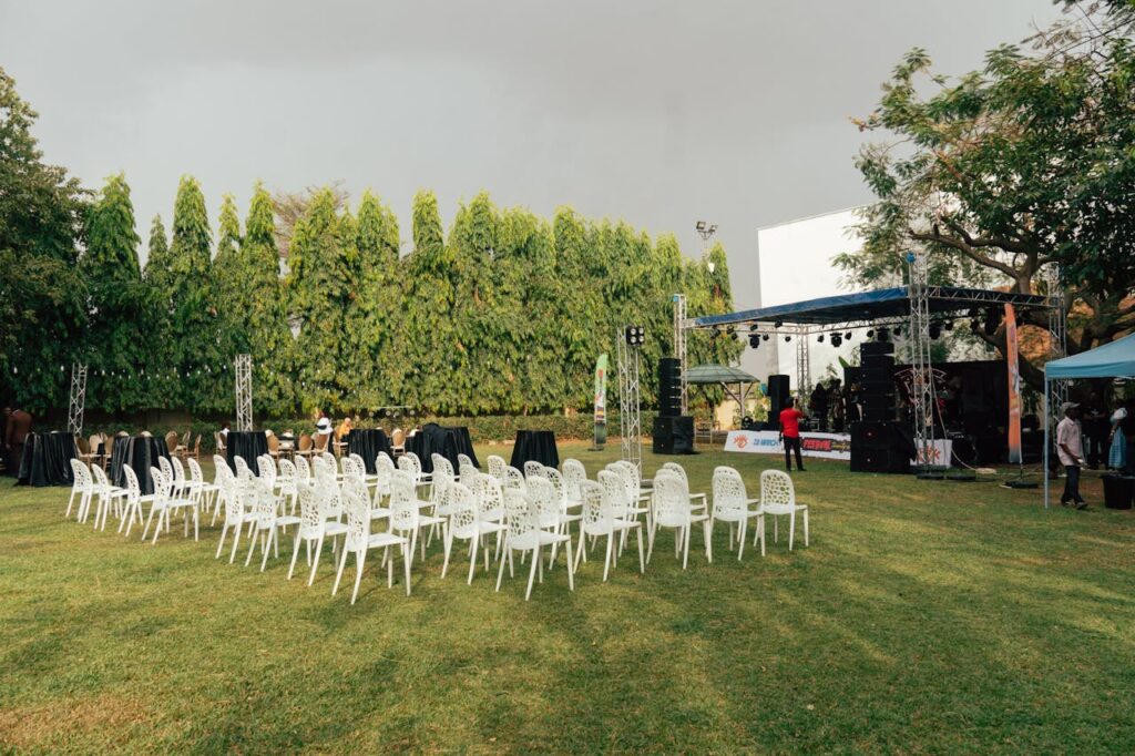 pexels-photo-36856348 An outdoor event venue with white chairs, stage setup, sound equipment, and greenery surrounding the space.